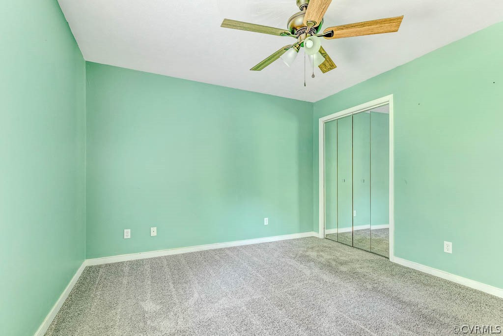 Empty bedroom with mint-green walls, gray carpet, mirrored closet doors, and a ceiling fan.