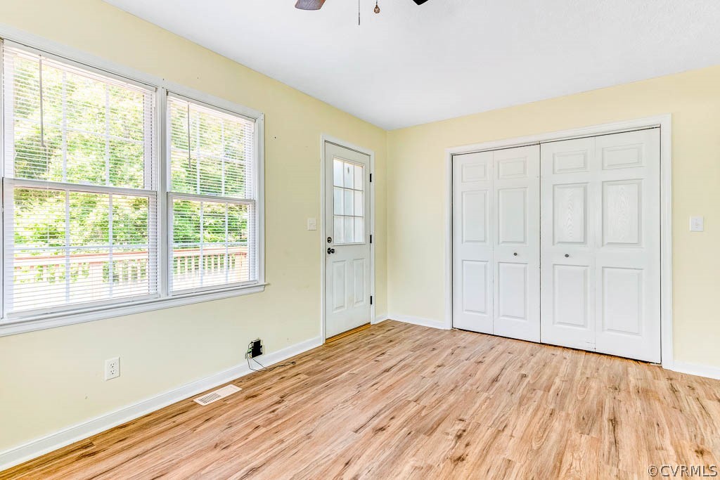 Empty bedroom with wood-look flooring, large windows, and white double closet doors.