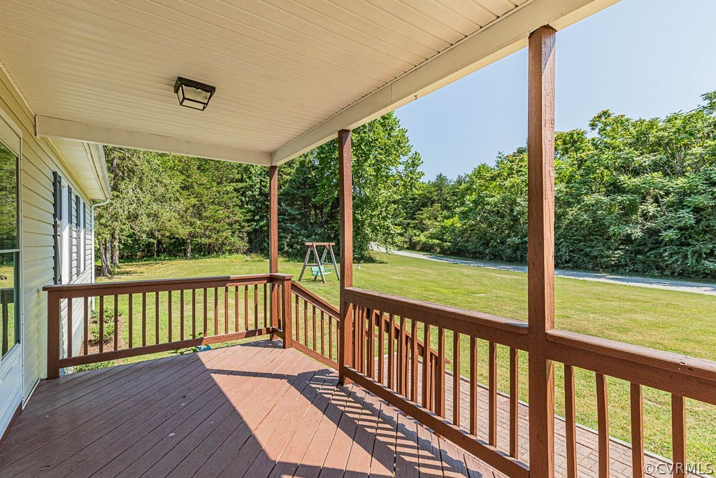 Covered wooden porch overlooking a lawn and wooded yard, with a swing set in the distance.