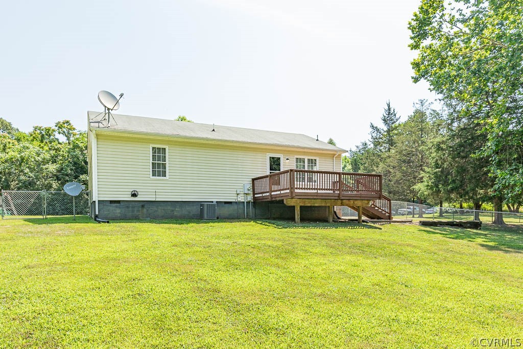 Rear exterior of a light-colored home with a raised deck and broad fenced lawn.