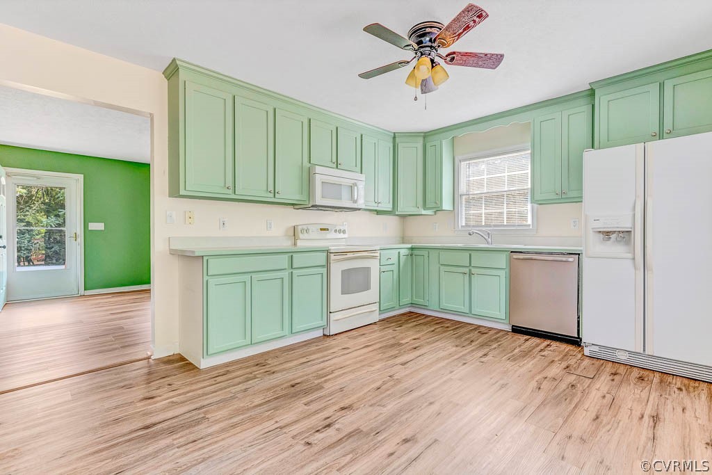 Vacant kitchen with pale green cabinets, white appliances, and wood-look flooring.