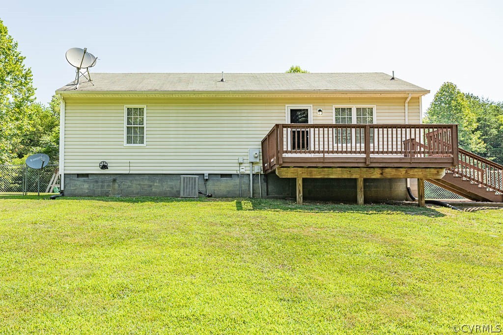 Rear of a light-colored house with a raised wooden deck and stairs overlooking a green lawn.