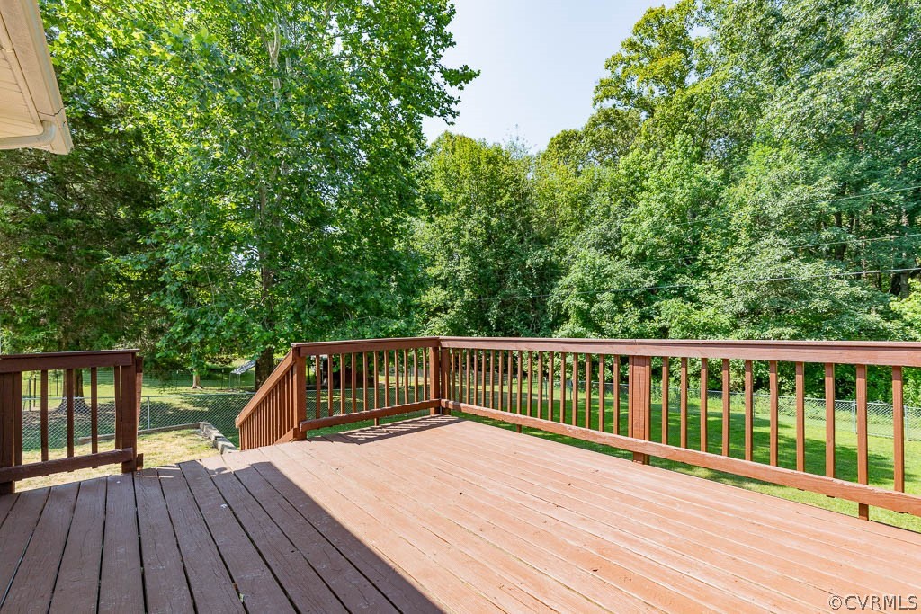 Wooden deck overlooking a green lawn bordered by mature trees.