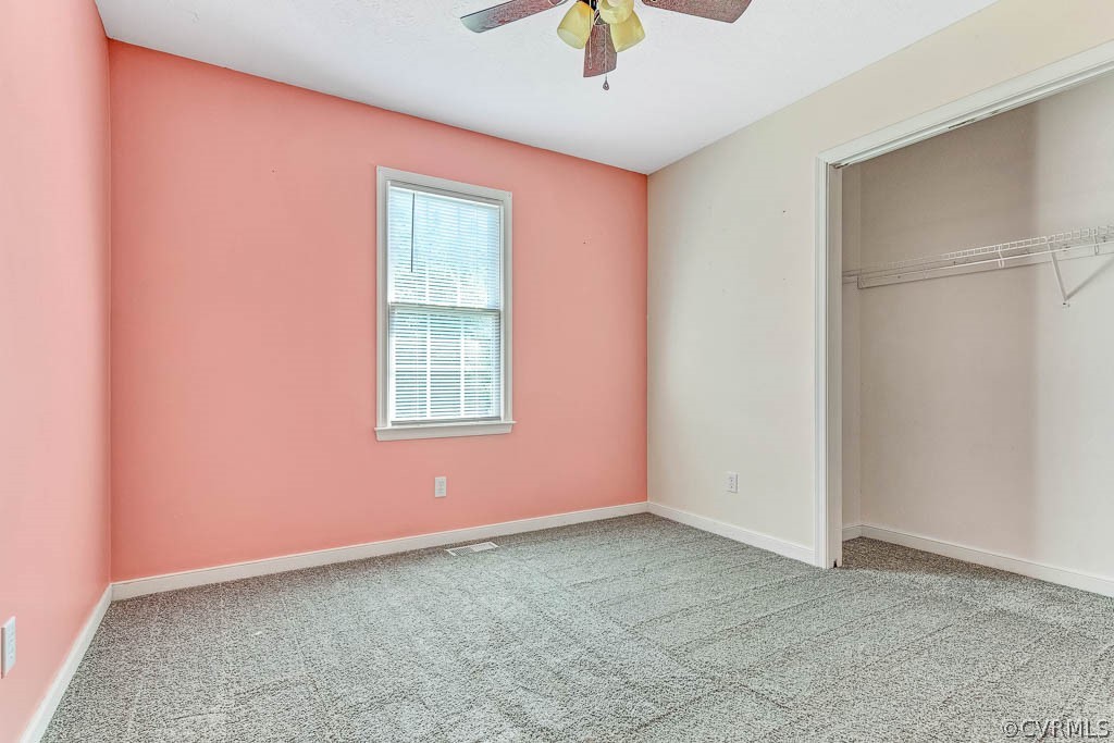 Empty bedroom with salmon-pink walls, gray carpet, a window, and an open closet.