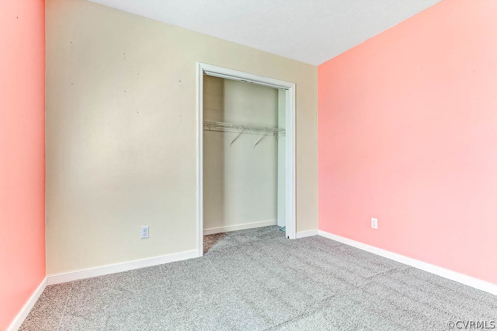 Empty bedroom with gray carpet, coral-pink walls, and an open closet.