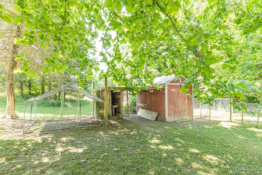 Backyard outbuildings beneath leafy trees, including a red shed and wire enclosure.