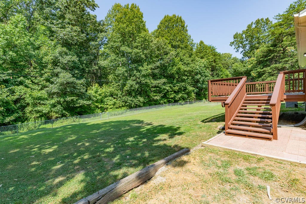 Backyard with a raised wooden deck and stairs beside a grassy lawn bordered by mature trees.