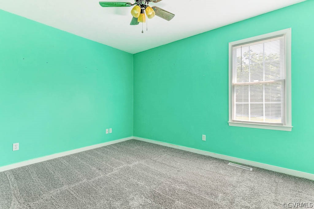 Empty bedroom with turquoise walls, gray carpet, one window with blinds, and a ceiling fan.