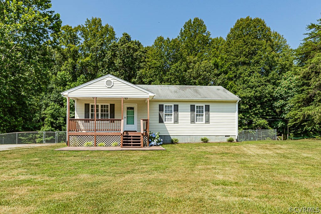 Single-story house with a covered front porch, broad lawn, and mature trees behind it.