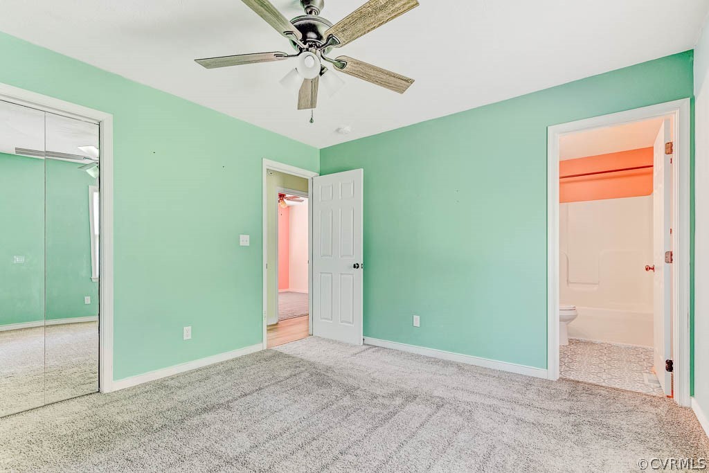 Empty mint-green bedroom with mirrored closet doors, ceiling fan, and adjoining bathroom.