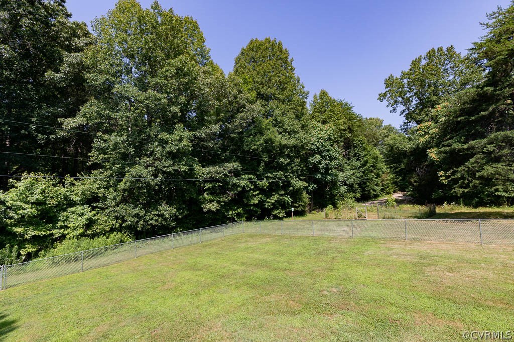 Grassy fenced yard bordered by dense trees, with a path opening through the woods.