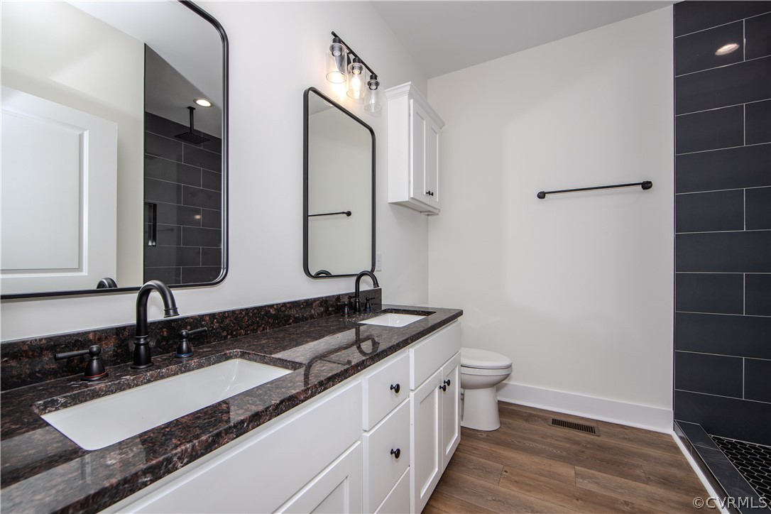 Bathroom with a double vanity, dark stone countertops, and a charcoal-tiled shower.
