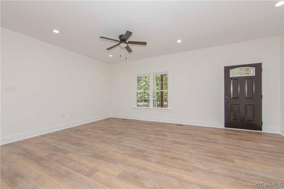 Vacant room with wood-look flooring, ceiling fan, window, and dark front door.