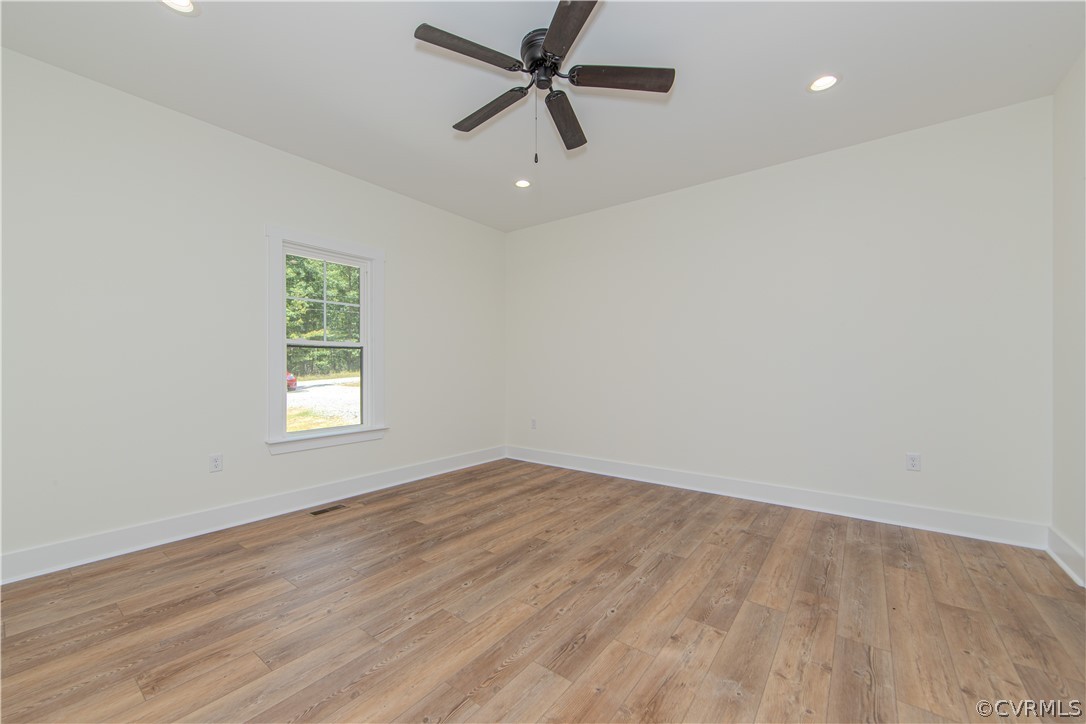 Vacant room with wide-plank wood flooring, a window, and a dark ceiling fan.