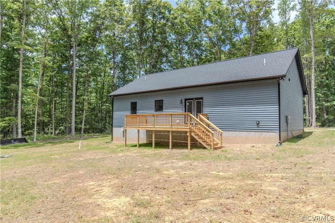 Gray-sided house with a raised wooden deck and stairs, surrounded by trees.