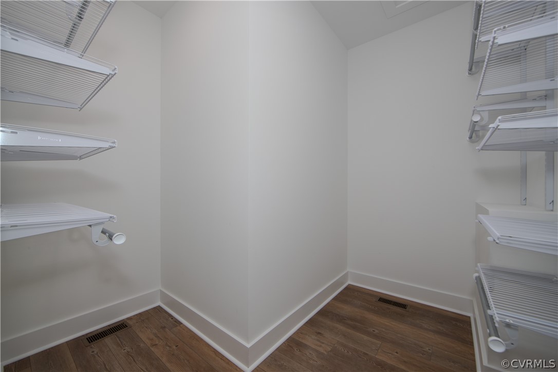Empty walk-in closet with white wire shelving and dark wood-look flooring.