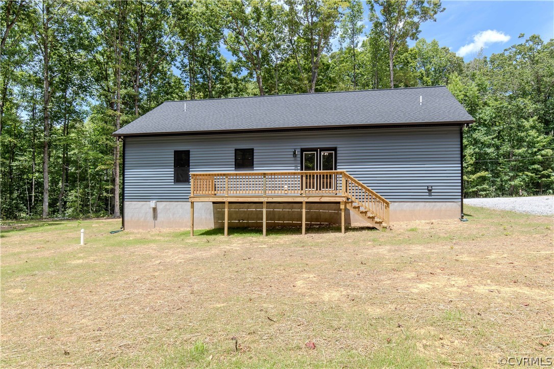 Rear of a gray-sided house with a raised wooden deck, surrounded by trees.