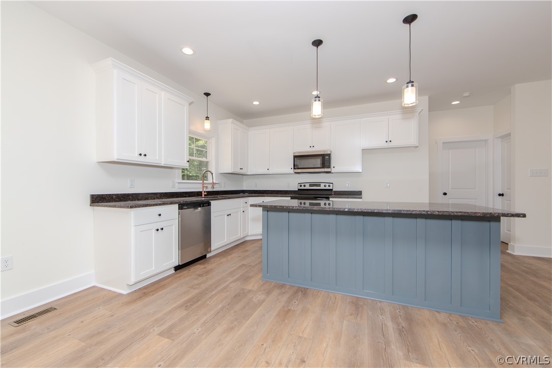 Kitchen with a large blue island, white cabinets, and stainless steel appliances.