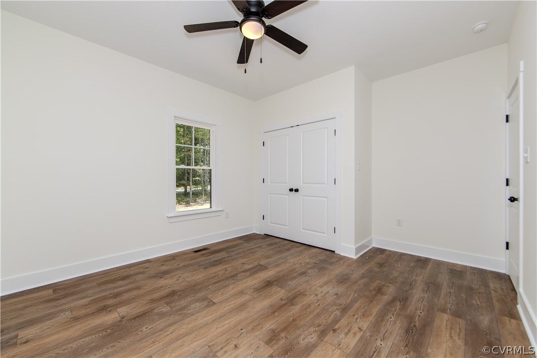 Empty room with brown wood-look flooring, double closet doors, and a ceiling fan.