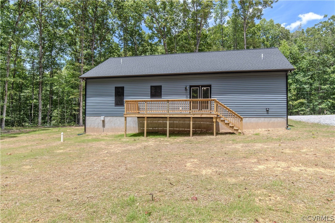 Rear of gray-sided house with a raised wooden deck and stairs, surrounded by a wooded lot.