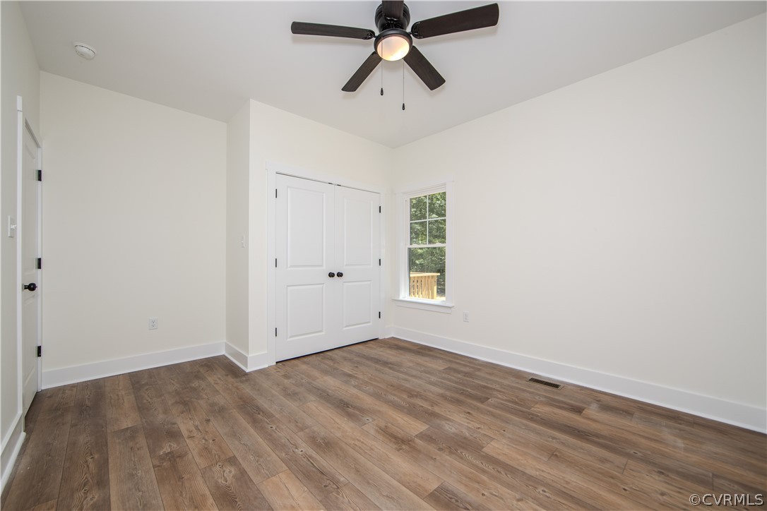 Empty bedroom with double closet doors, wood-look flooring, a window, and a ceiling fan.