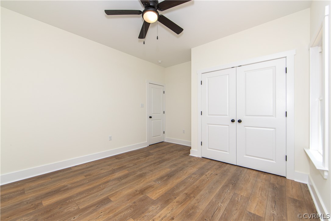 Empty bedroom with wood plank flooring, double closet doors, and a ceiling fan.