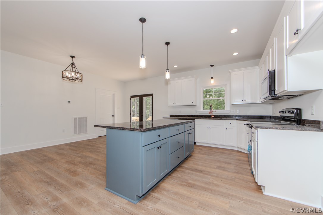 Kitchen with a blue island, white cabinets, dark countertops, and wood floors.