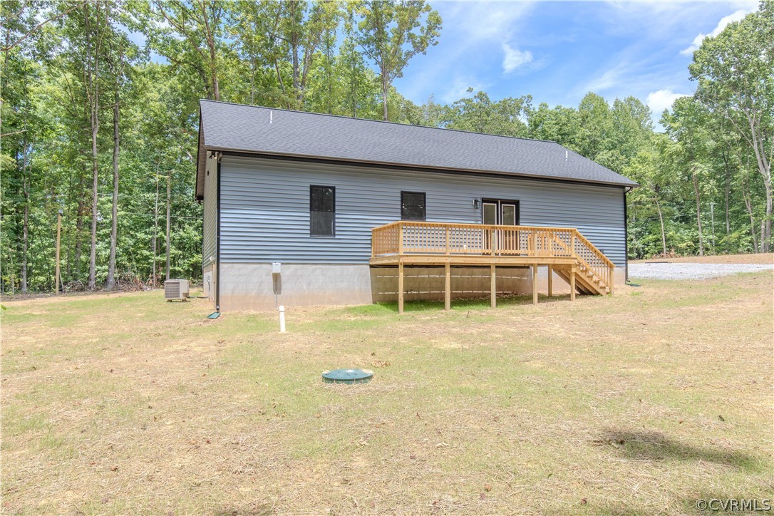 Gray-sided home with a raised wooden deck and stairs, surrounded by mature trees.