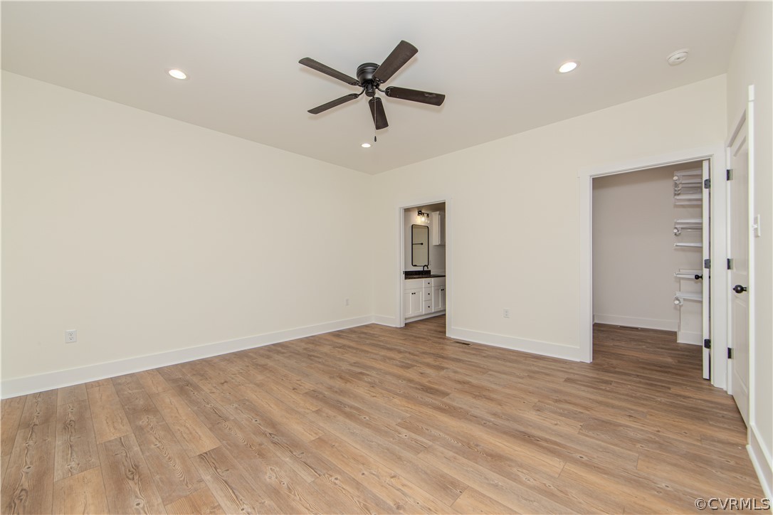 Empty bedroom with wood-look flooring, a ceiling fan, and doorways to a bathroom and closet.