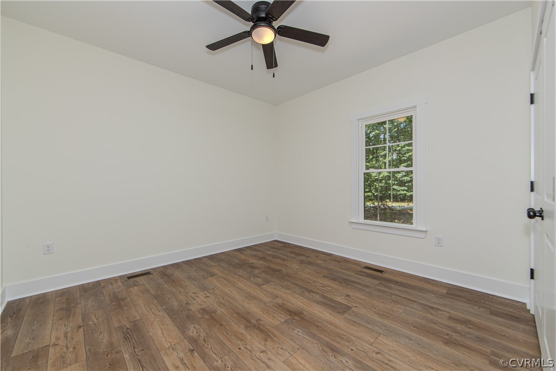 Empty bedroom with wood-look flooring, a ceiling fan, and a window overlooking trees.
