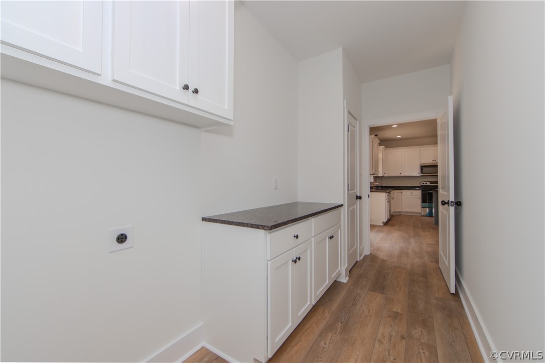 Cabinet-lined passage with a dark countertop leads into a white kitchen with wood-look flooring.
