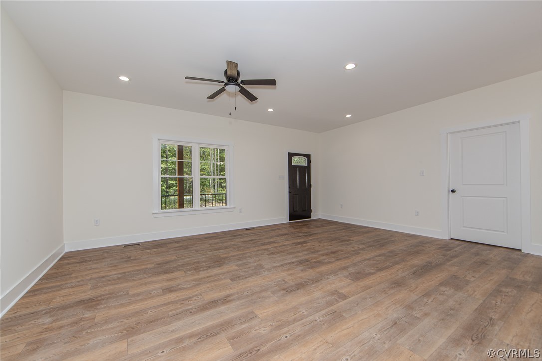 Vacant room with wide-plank flooring, a ceiling fan, and a large window overlooking trees.