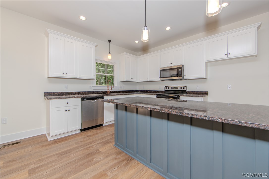 Kitchen with a blue island, white cabinets, dark stone counters, and stainless steel appliances.