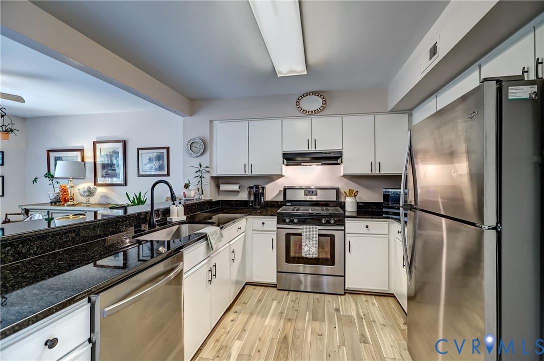 Kitchen with white cabinets, black granite counters, stainless steel appliances, and light wood-look flooring.