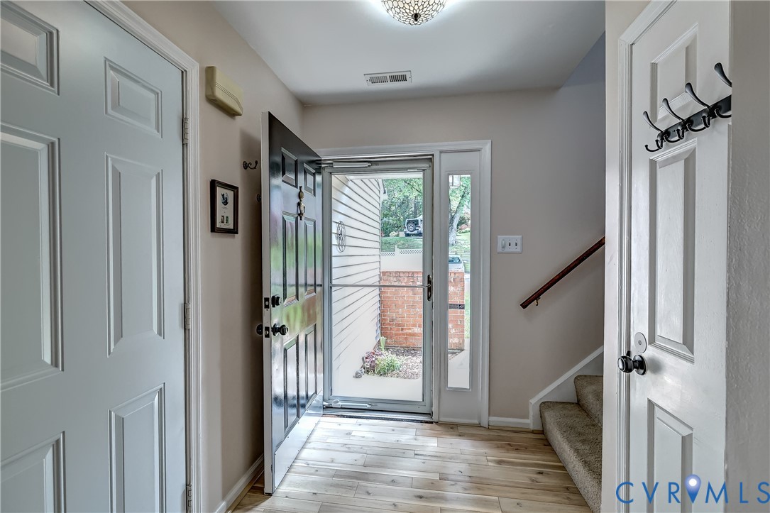 Entryway with open front door, glass storm door, light wood flooring, and carpeted staircase.