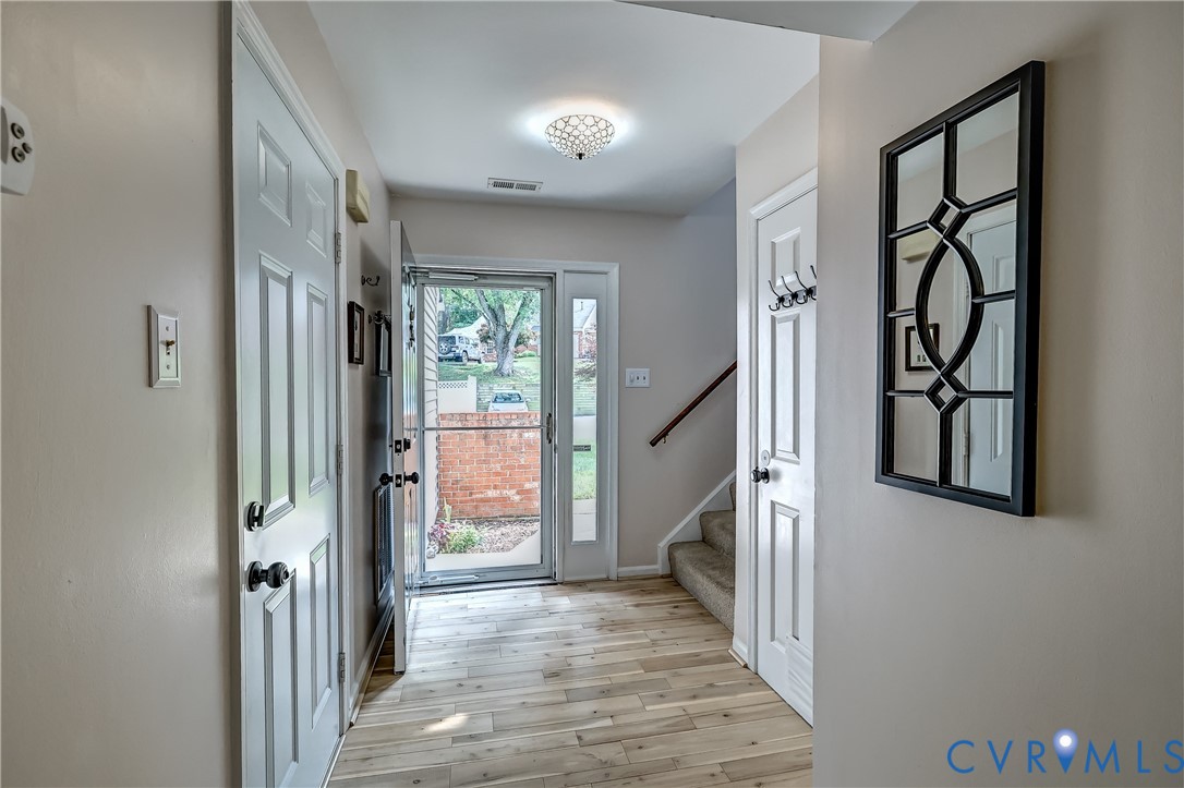 Entryway with light wood-plank flooring, a glass front door, stairs, and a decorative wall mirror.