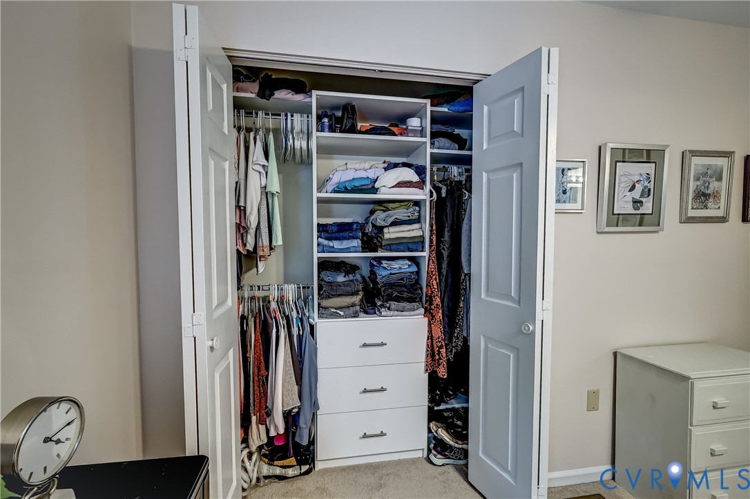 Open bedroom closet with hanging clothes, folded garments, and built-in drawers.