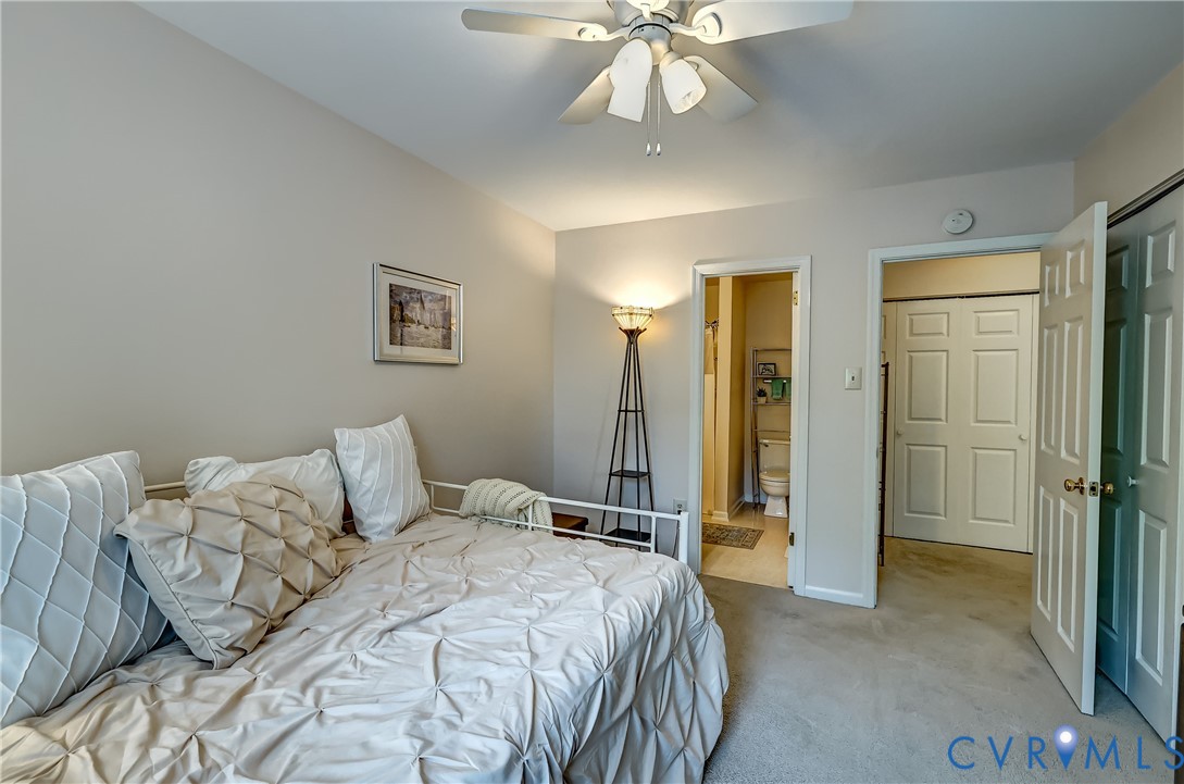 Bedroom with a white quilted bed, ceiling fan, and open bathroom doorway.