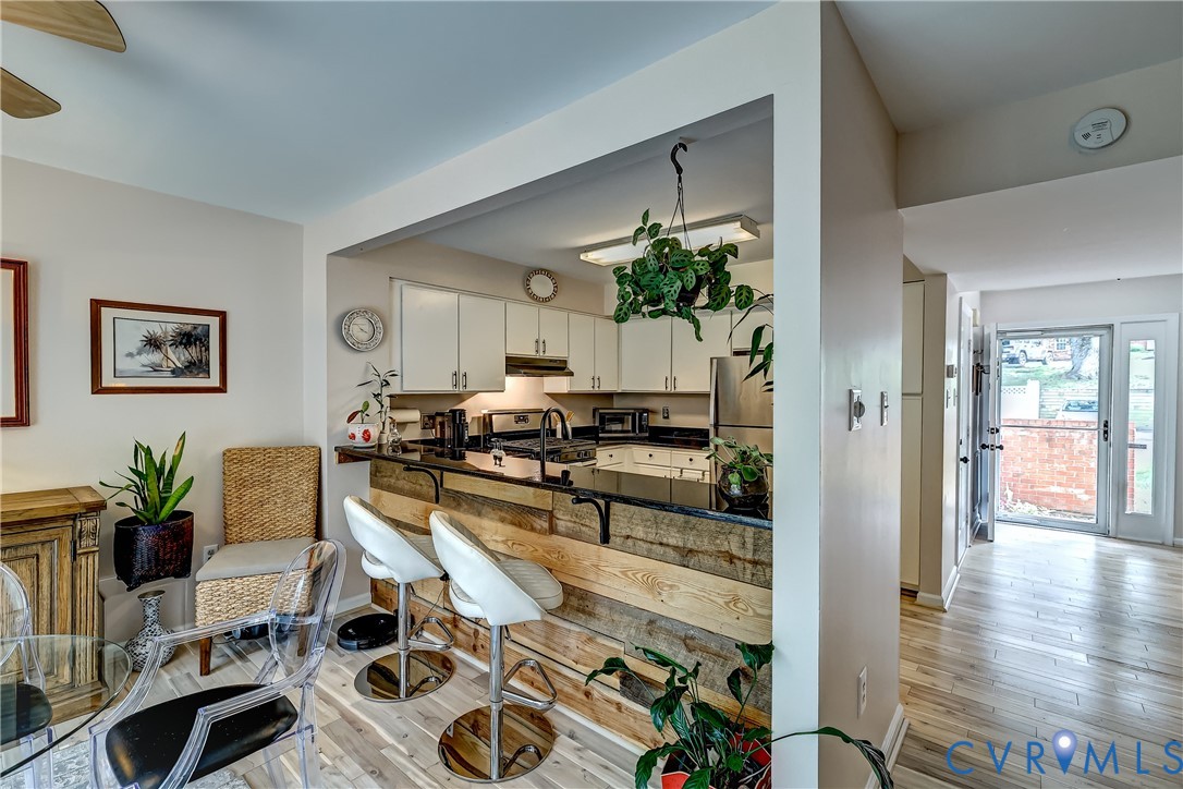 Kitchen and dining area with a rustic wood breakfast bar, white stools, and glass dining table.