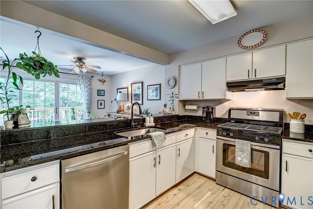 Kitchen with dark granite counters, white cabinets, stainless appliances, and an adjoining bright sitting area.