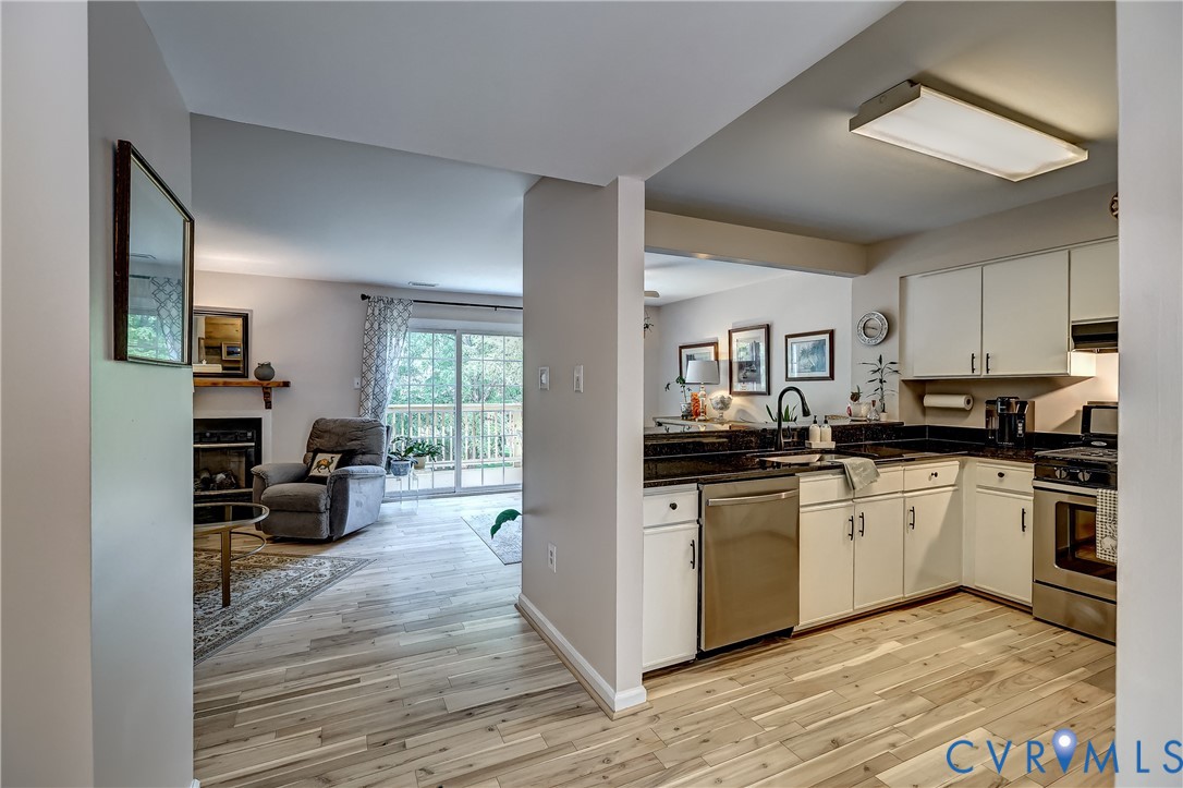 Open kitchen with white cabinets and stainless steel appliances beside a living area with a fireplace and sliding doors.