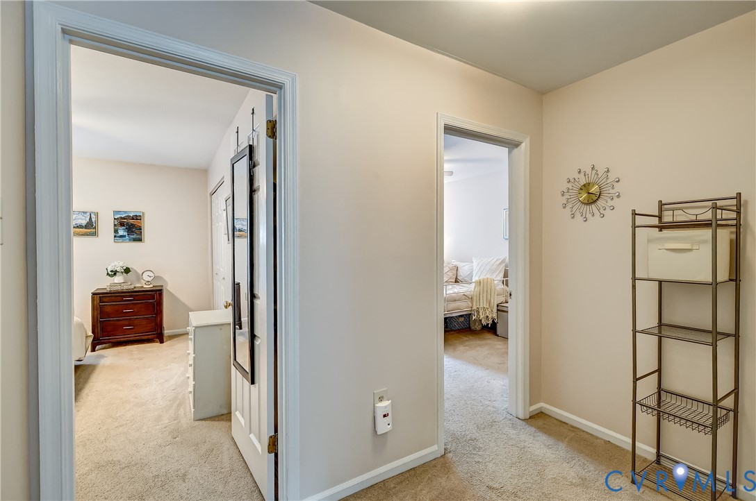 Carpeted hallway with open doorways into two furnished rooms and a metal storage rack.
