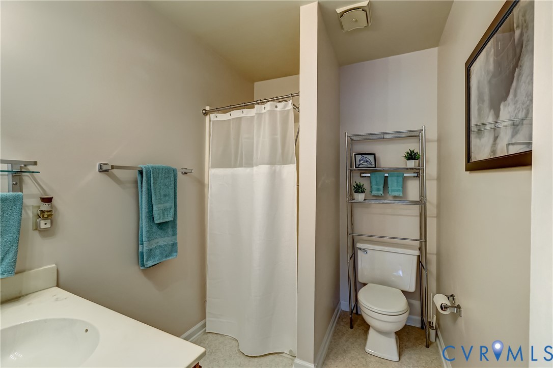 Bathroom with a white shower curtain, vanity sink, and toilet beside chrome shelving.