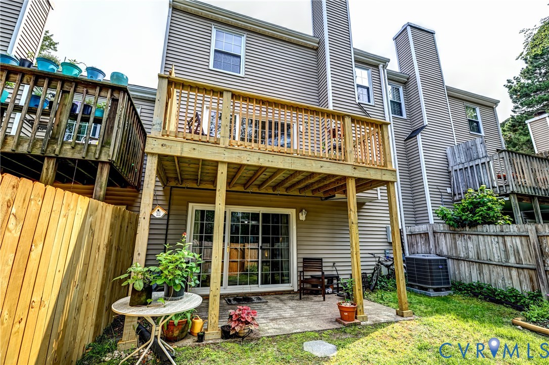 Rear of a gray-sided home with a raised wooden deck and a covered patio in a fenced yard.