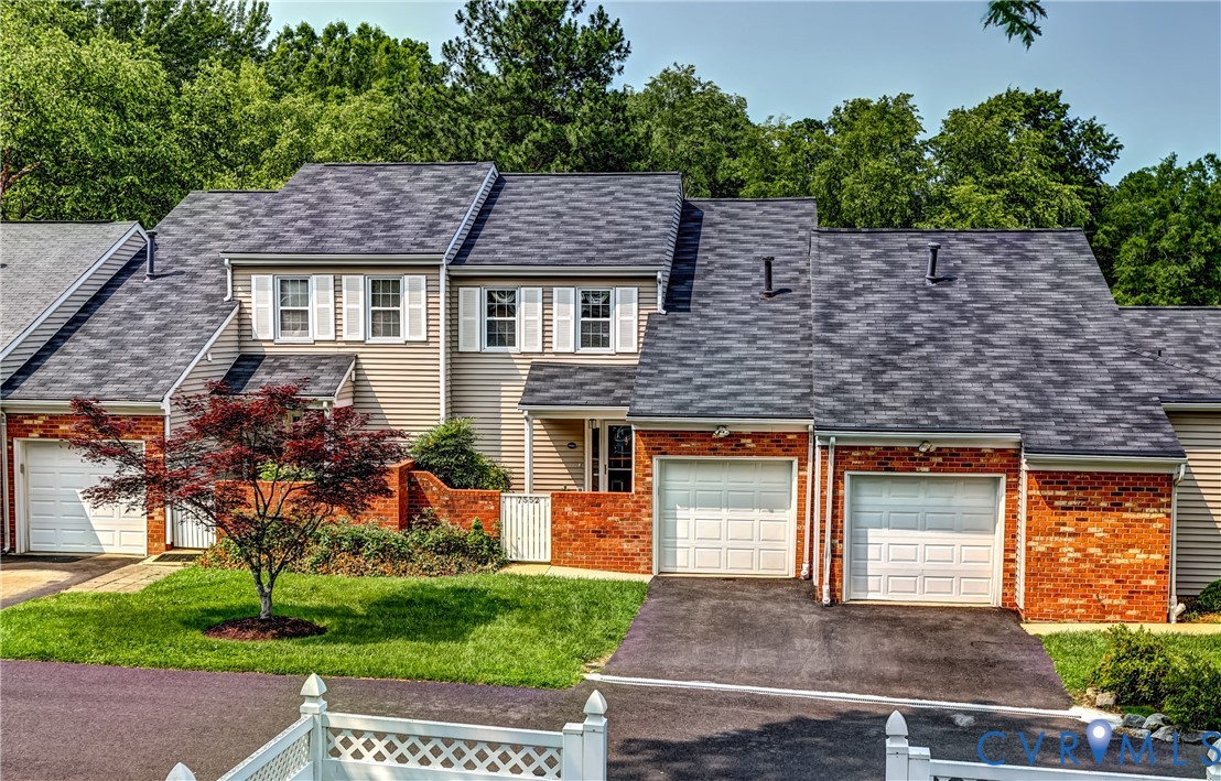 Attached home with tan siding, red brick accents, multiple garage doors, and a small front lawn.