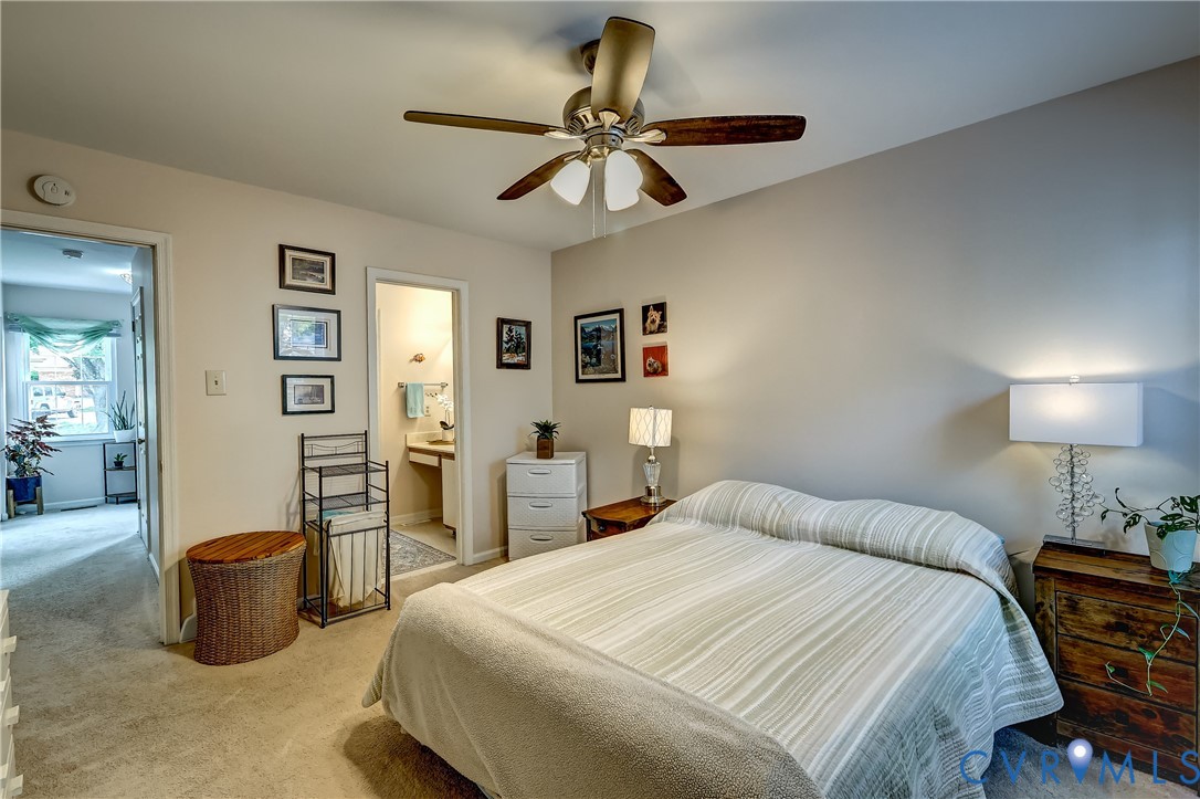 Furnished bedroom with a large striped bed, ceiling fan, and open doorway to an en-suite bathroom.