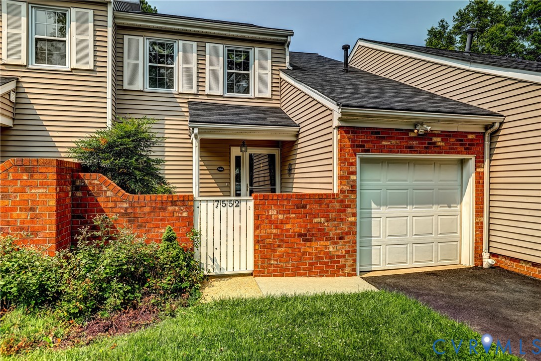 Two-story house with beige siding, red brick accents, a gated entry, and attached garage.