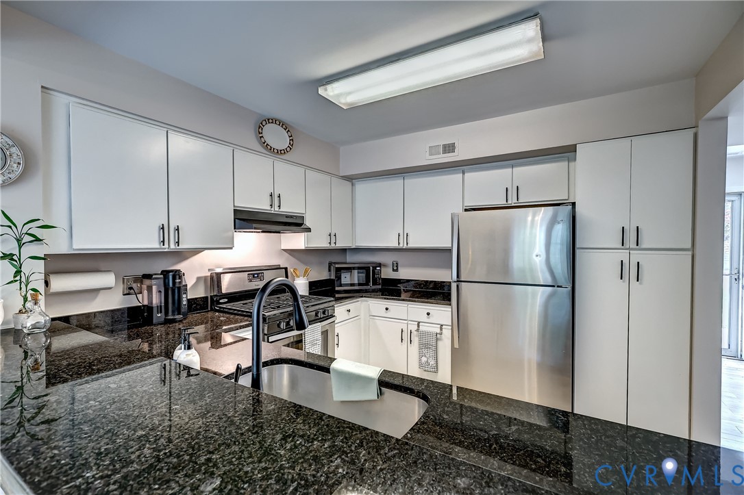 Kitchen with white cabinets, dark granite counters, stainless steel appliances, and a peninsula sink.