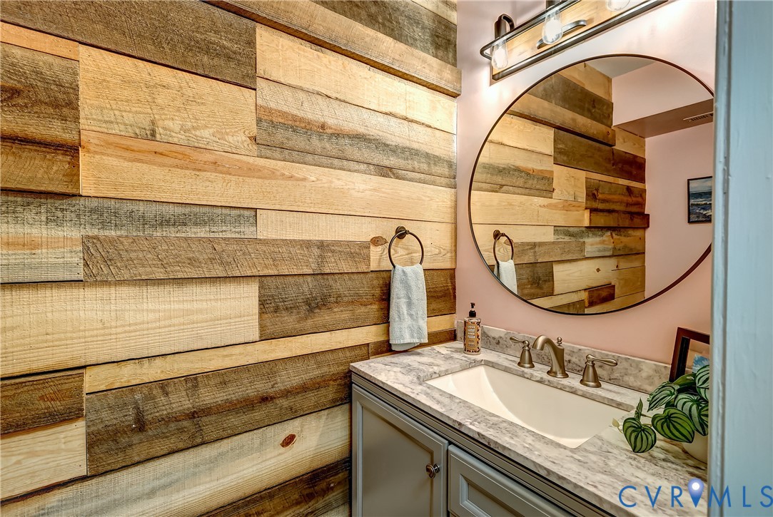 Bathroom vanity with a round mirror and a wall of multicolored reclaimed-wood planks.