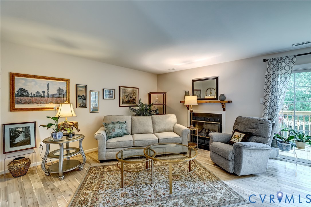 Staged living room with a beige sofa, gray recliner, fireplace, and sliding glass door to a balcony.